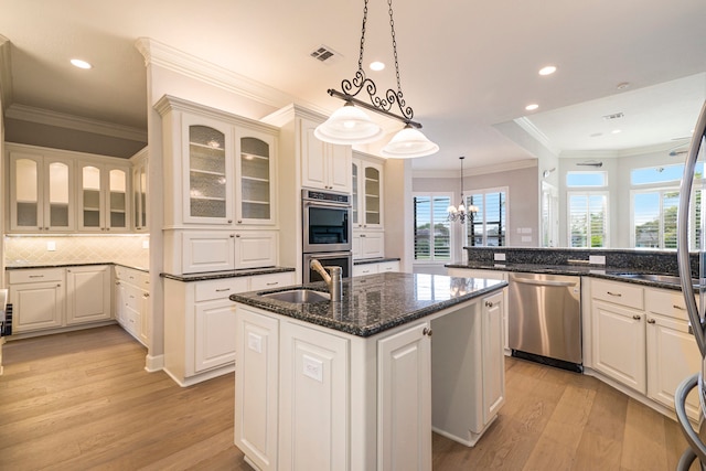 kitchen with an island with sink, light hardwood / wood-style flooring, sink, pendant lighting, and stainless steel appliances