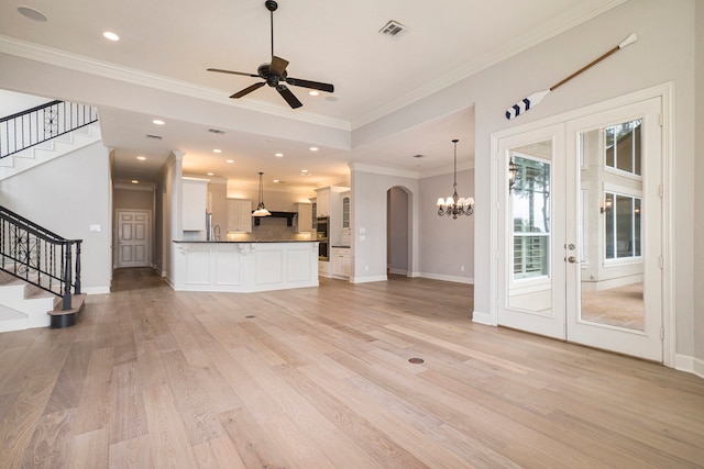 unfurnished living room with light wood-type flooring, ornamental molding, ceiling fan with notable chandelier, french doors, and sink