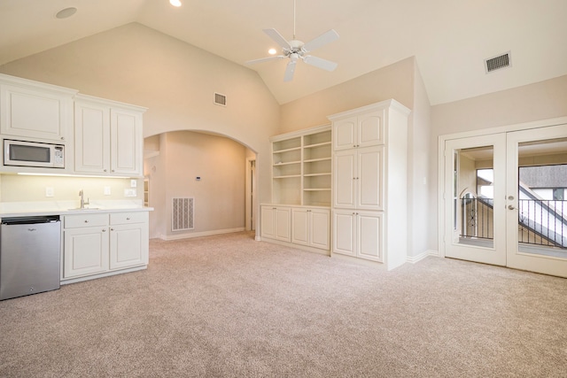 unfurnished living room featuring sink, french doors, ceiling fan, high vaulted ceiling, and light colored carpet