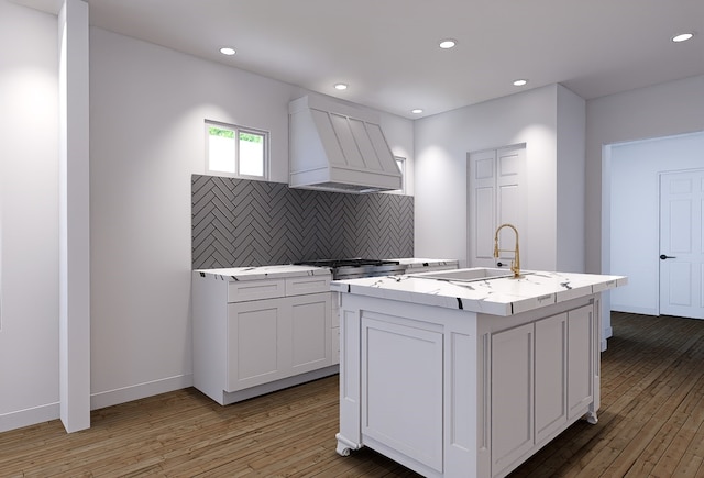 kitchen featuring sink, an island with sink, hardwood / wood-style floors, white cabinetry, and premium range hood