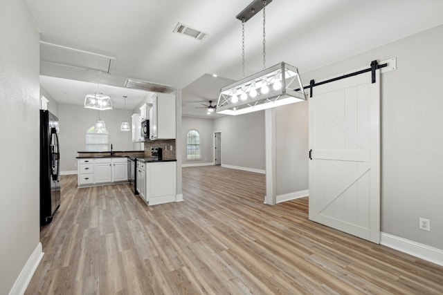 kitchen with white cabinetry, ceiling fan, stainless steel appliances, a barn door, and decorative light fixtures