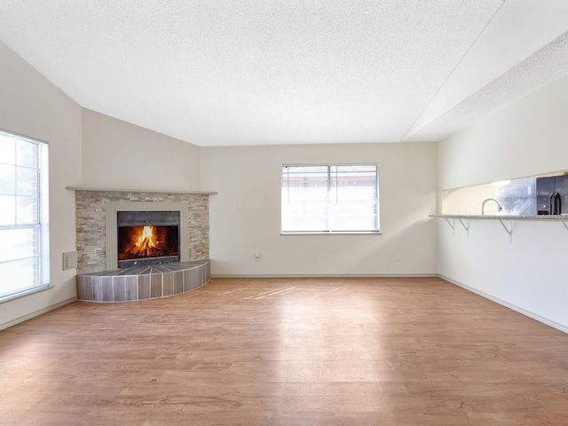 unfurnished living room featuring vaulted ceiling, a fireplace, a textured ceiling, and light hardwood / wood-style floors