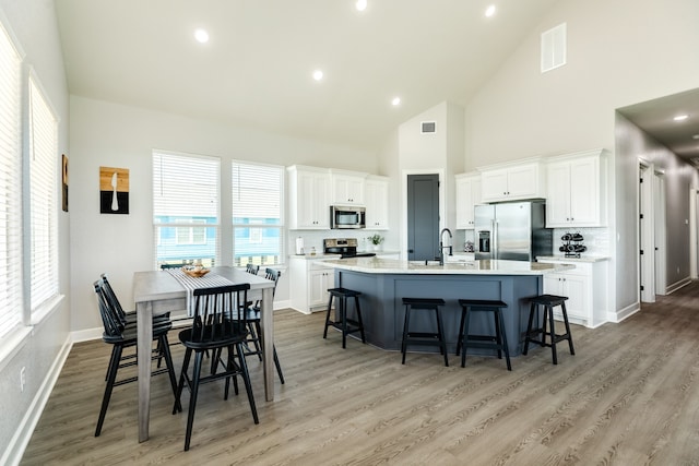 kitchen featuring hardwood / wood-style floors, white cabinetry, stainless steel appliances, and an island with sink