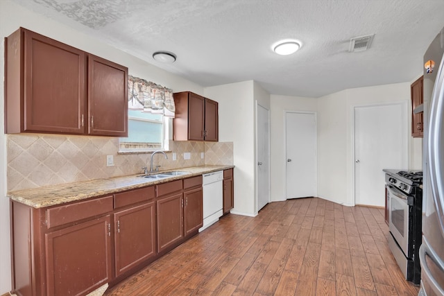 kitchen featuring white dishwasher, sink, hardwood / wood-style floors, a textured ceiling, and gas stove