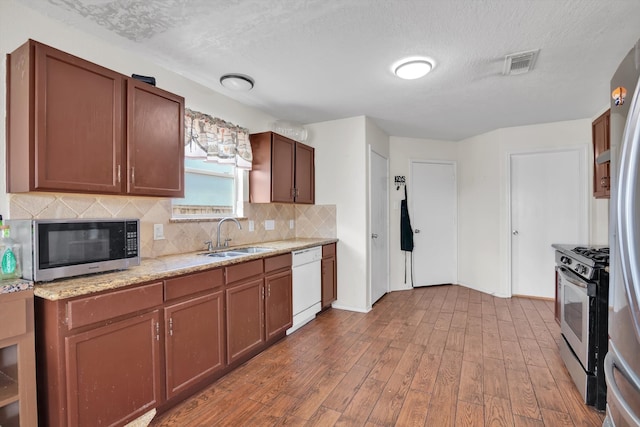 kitchen with light stone countertops, sink, wood-type flooring, a textured ceiling, and stainless steel appliances