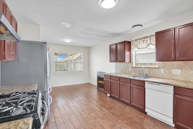 kitchen with sink, dishwasher, light wood-type flooring, stainless steel range with gas cooktop, and range hood