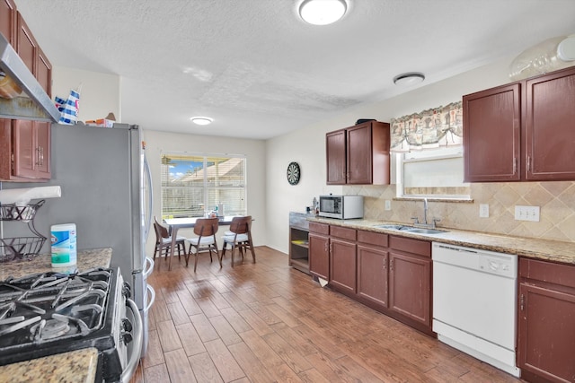 kitchen featuring stainless steel appliances, backsplash, wood-type flooring, sink, and light stone counters