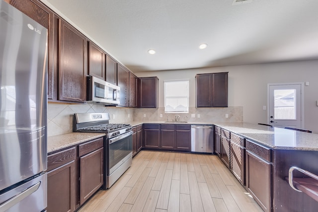 kitchen featuring decorative backsplash, appliances with stainless steel finishes, light stone counters, and kitchen peninsula