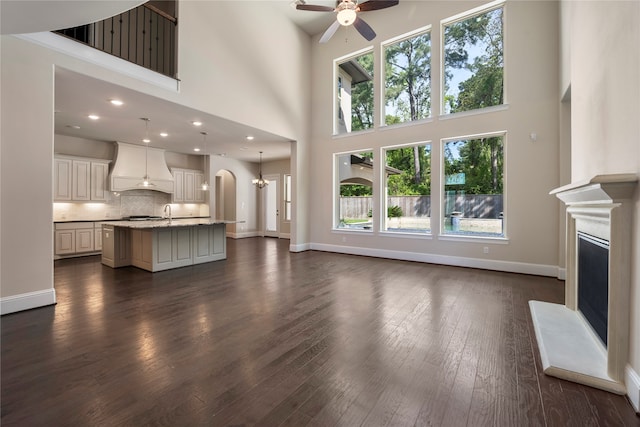 unfurnished living room featuring ceiling fan with notable chandelier, a towering ceiling, and dark wood-type flooring