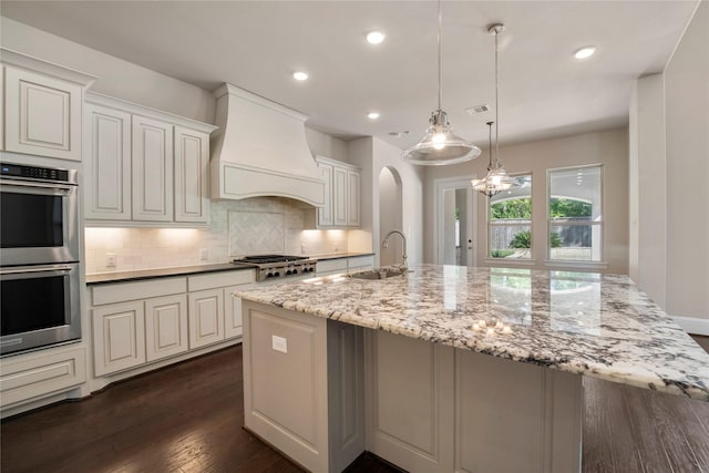 kitchen featuring appliances with stainless steel finishes, a sink, premium range hood, tasteful backsplash, and arched walkways
