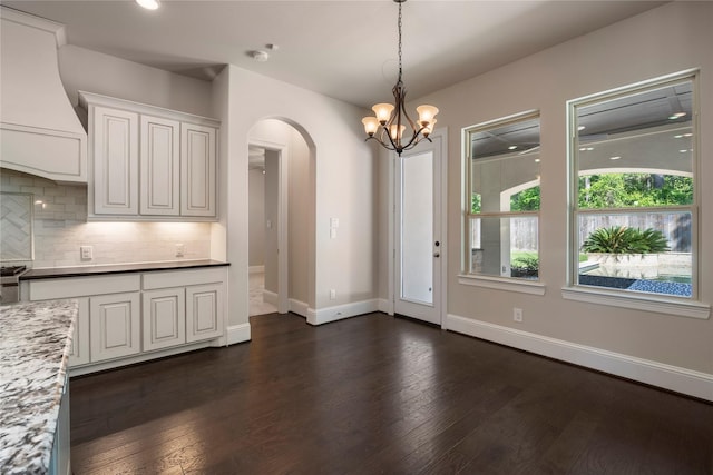 unfurnished dining area with arched walkways, dark wood finished floors, baseboards, a chandelier, and recessed lighting