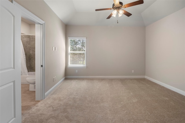 unfurnished bedroom featuring lofted ceiling, baseboards, ensuite bathroom, light carpet, and ceiling fan