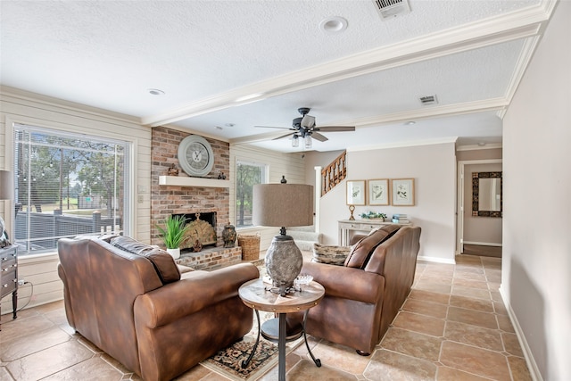 living room with beam ceiling, crown molding, a brick fireplace, a textured ceiling, and ceiling fan