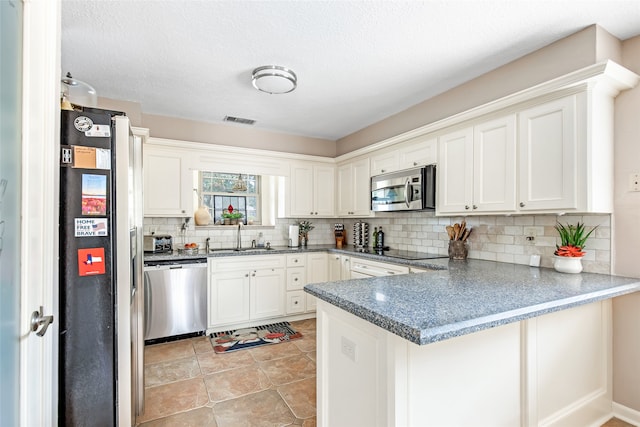 kitchen with kitchen peninsula, backsplash, sink, white cabinetry, and appliances with stainless steel finishes