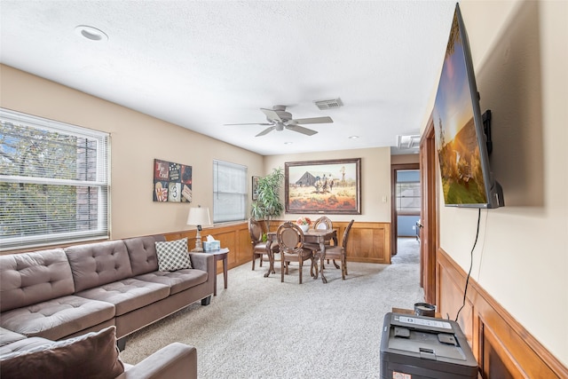 carpeted living room featuring ceiling fan, a textured ceiling, plenty of natural light, and wooden walls