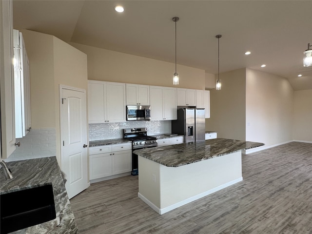 kitchen with white cabinets, a kitchen island, stainless steel appliances, dark stone countertops, and hanging light fixtures