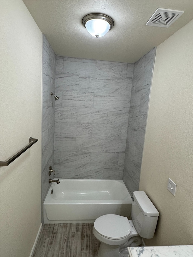 bathroom featuring hardwood / wood-style flooring, a textured ceiling, toilet, and tiled shower / bath combo