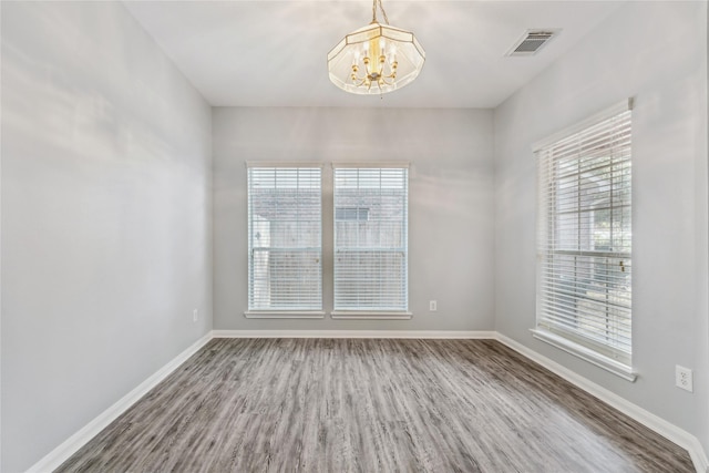 empty room featuring hardwood / wood-style flooring, plenty of natural light, and an inviting chandelier