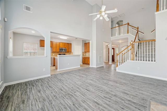 unfurnished living room with light hardwood / wood-style flooring, ceiling fan, and a high ceiling