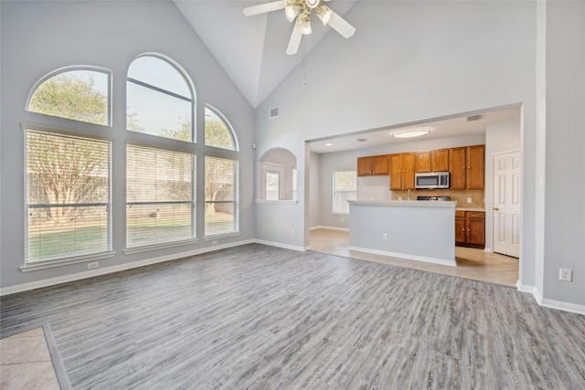 unfurnished living room with high vaulted ceiling, ceiling fan, and light wood-type flooring