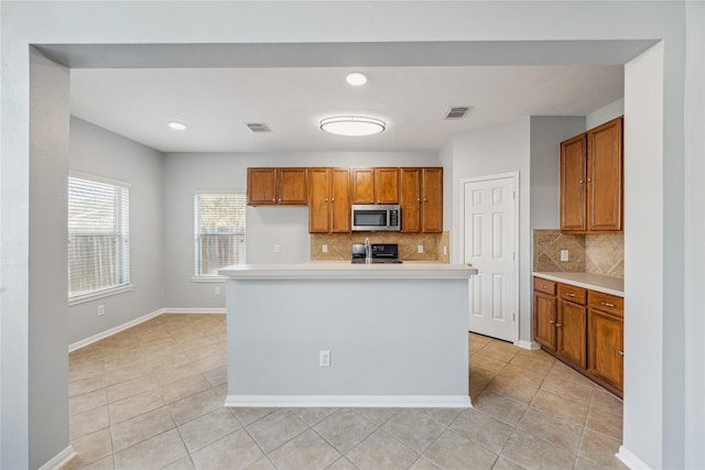 kitchen with decorative backsplash, a center island with sink, and range with electric stovetop