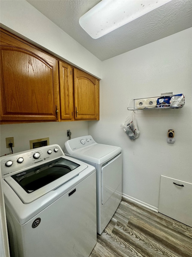 laundry room featuring hardwood / wood-style floors, washer and clothes dryer, a textured ceiling, and cabinets