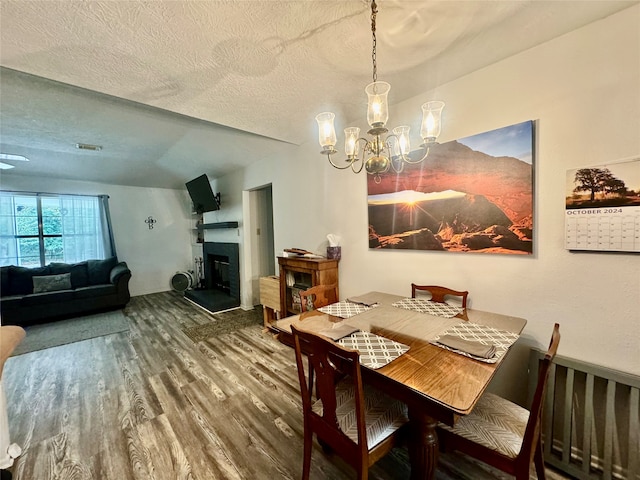 dining space with a notable chandelier, wood-type flooring, a textured ceiling, and a fireplace