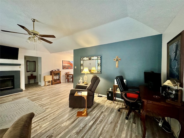 living room with ceiling fan, a textured ceiling, vaulted ceiling, and light wood-type flooring