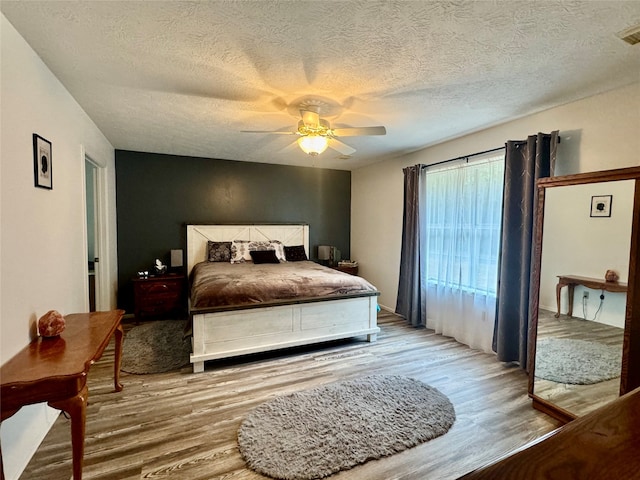 bedroom with a textured ceiling, wood-type flooring, and ceiling fan