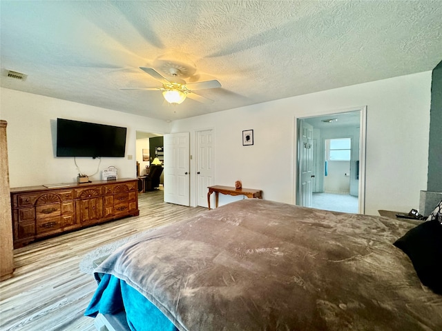 bedroom with ceiling fan, ensuite bath, a textured ceiling, and light hardwood / wood-style floors