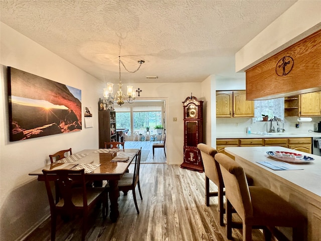 dining room featuring a notable chandelier, a textured ceiling, sink, and light wood-type flooring