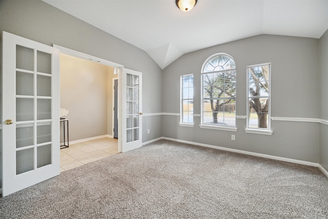 spare room featuring french doors, light colored carpet, and vaulted ceiling