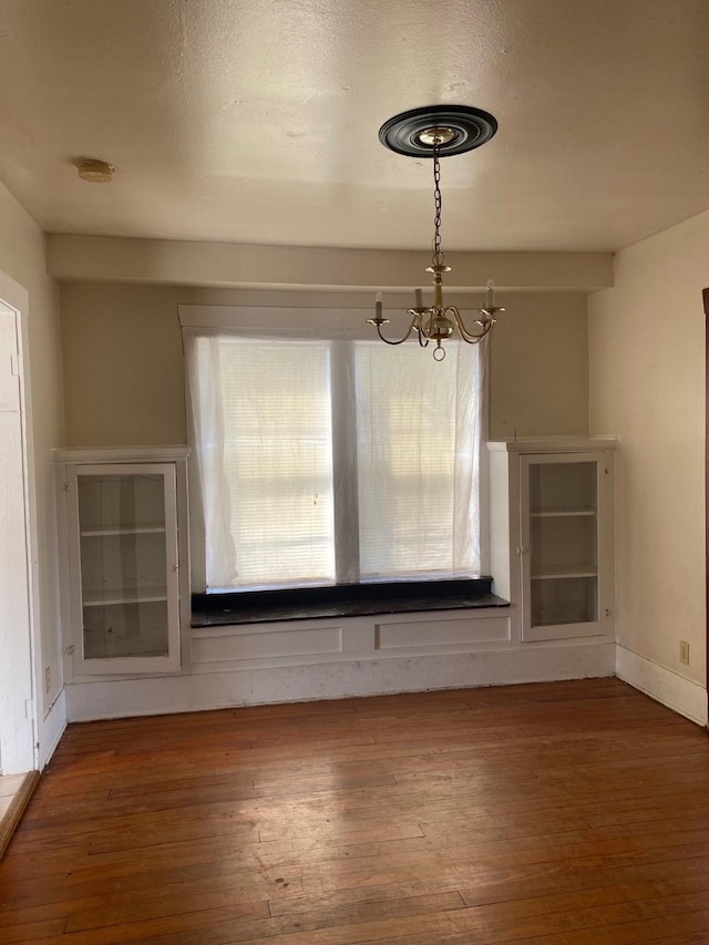 unfurnished dining area with a chandelier, dark wood-style flooring, a textured ceiling, and baseboards