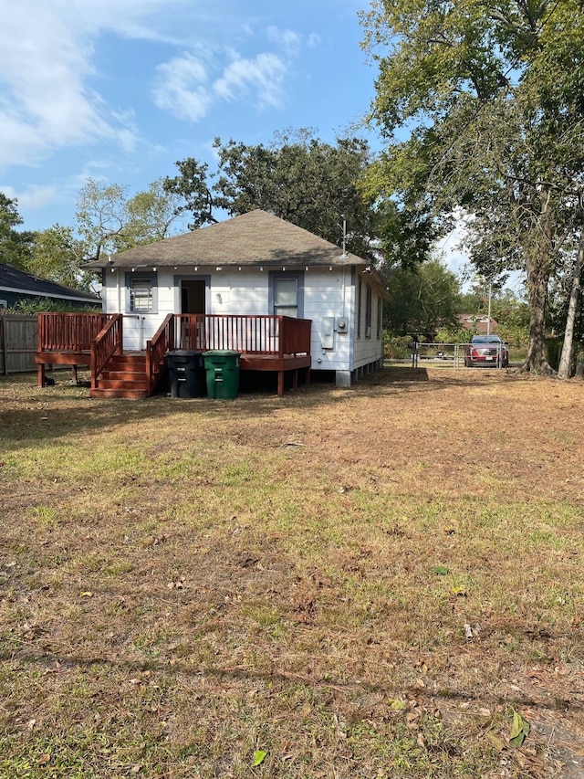 rear view of house with a shingled roof, fence, a deck, and a yard