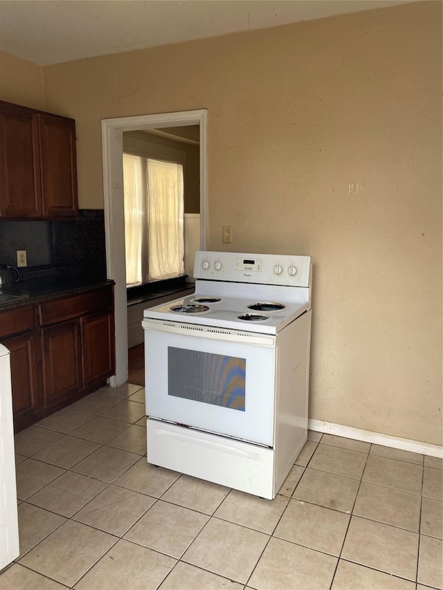 kitchen featuring dark countertops, light tile patterned floors, baseboards, and white range with electric cooktop