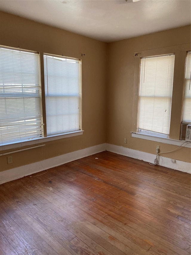 unfurnished room with plenty of natural light, wood finished floors, and baseboards