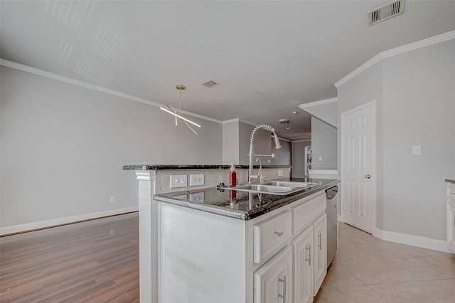 kitchen with stainless steel dishwasher, sink, white cabinets, a kitchen island with sink, and ornamental molding