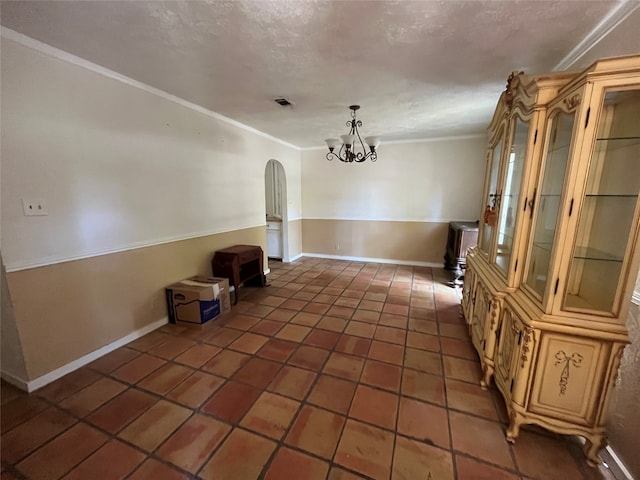 unfurnished dining area with a notable chandelier, ornamental molding, a textured ceiling, and dark tile patterned flooring