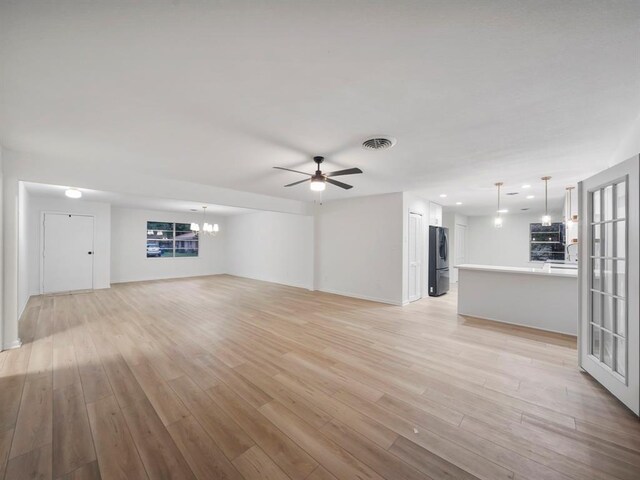 unfurnished living room with ceiling fan with notable chandelier, visible vents, and light wood-type flooring