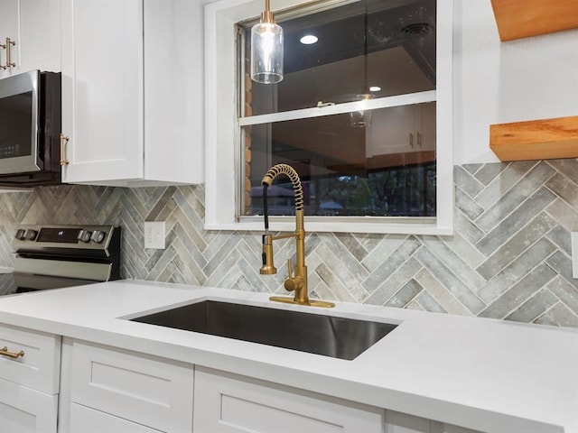 kitchen with backsplash, hanging light fixtures, sink, appliances with stainless steel finishes, and white cabinetry