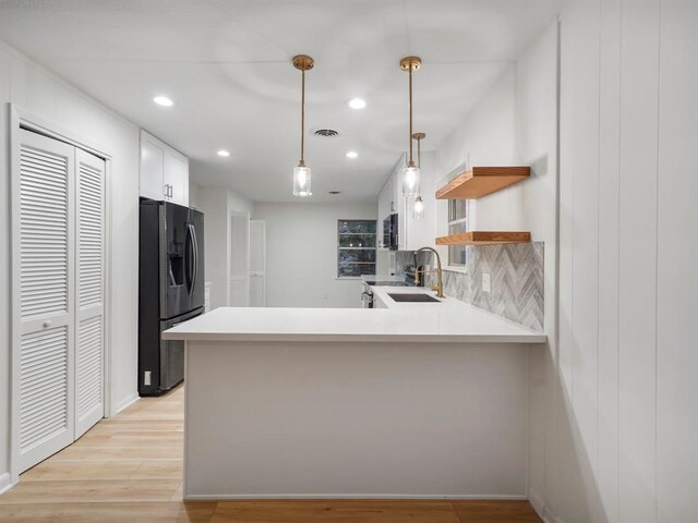 kitchen with white cabinets, hanging light fixtures, decorative backsplash, refrigerator with ice dispenser, and kitchen peninsula