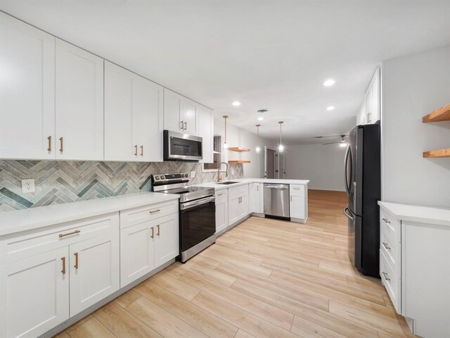 kitchen featuring pendant lighting, sink, kitchen peninsula, appliances with stainless steel finishes, and white cabinetry