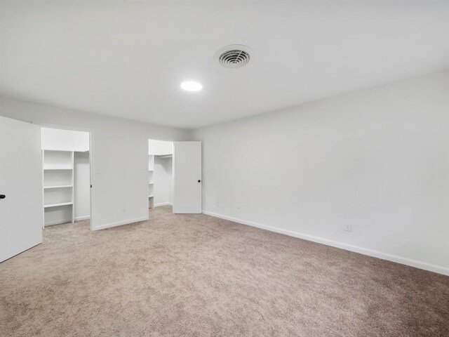 unfurnished bedroom featuring a walk in closet, carpet, visible vents, and baseboards