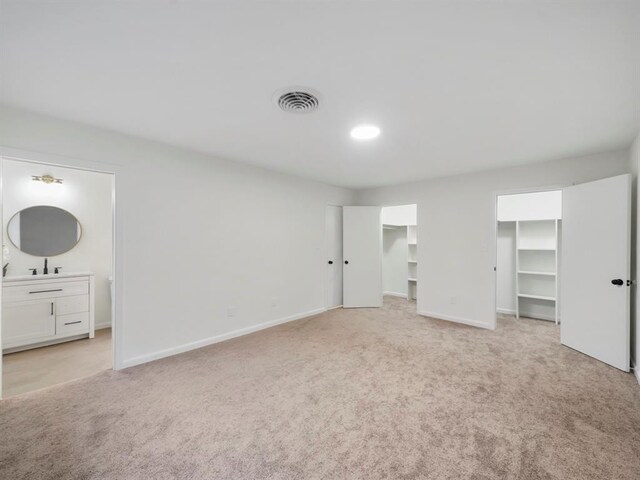 unfurnished bedroom with visible vents, light carpet, ensuite bathroom, a sink, and baseboards