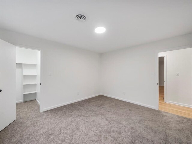 unfurnished bedroom featuring baseboards, a walk in closet, carpet floors, and visible vents