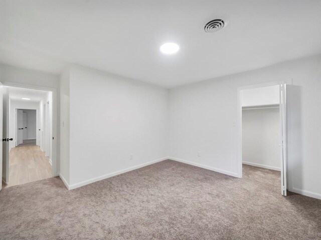 unfurnished bedroom with a spacious closet, visible vents, baseboards, carpet, and a closet