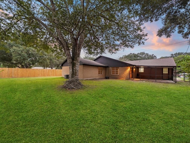 back of house at dusk featuring a yard, fence, and brick siding