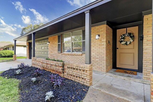 entrance to property featuring brick siding, a porch, concrete driveway, and a garage