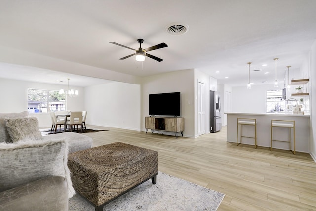 living room with visible vents, baseboards, recessed lighting, light wood-style floors, and ceiling fan with notable chandelier