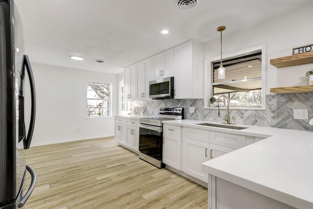 kitchen with visible vents, light wood-style flooring, a sink, stainless steel appliances, and decorative backsplash